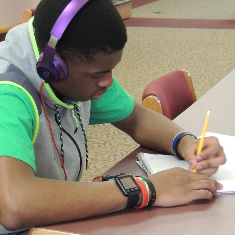 student with headphones on while writing in a notepad